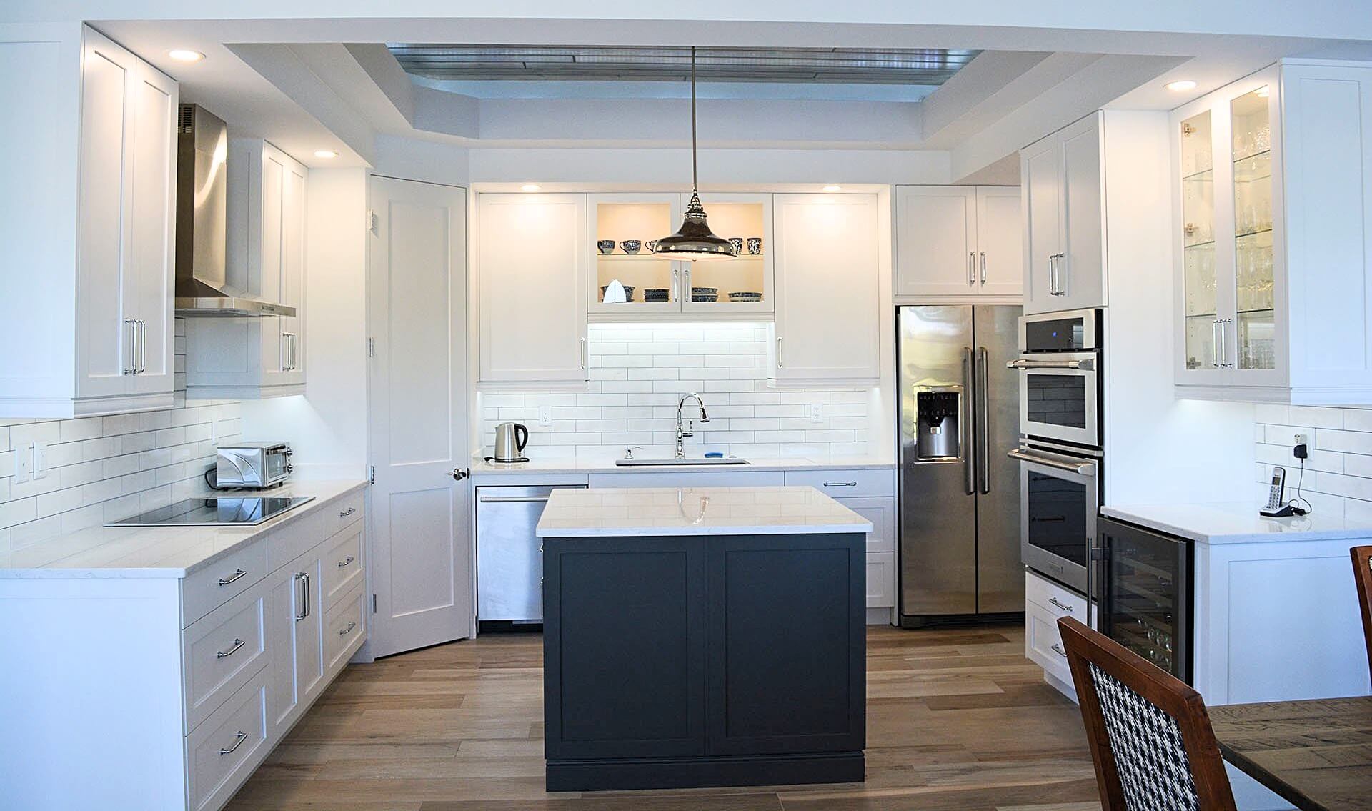 Condo kitchen with navy island, white cabinetry, glass-front uppers and double wall ovens