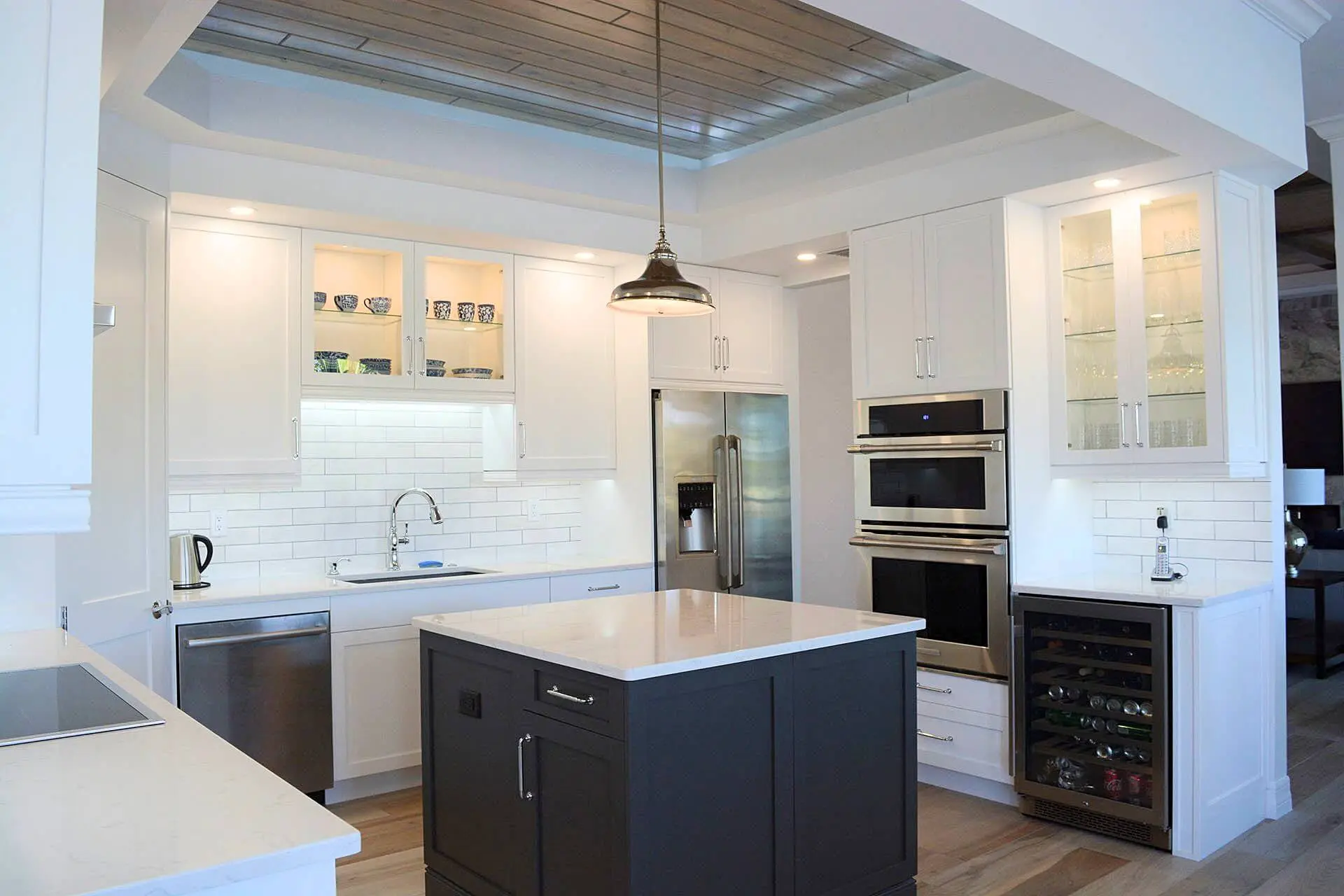 Condo kitchen with a navy island, white cabinetry and lit glass-front uppers
