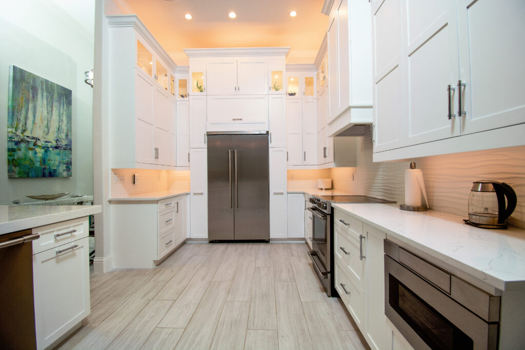Structural kitchen renovation in Pelican Bay, Naples, with full-height white shaker cabinetry and lit glass uppers
