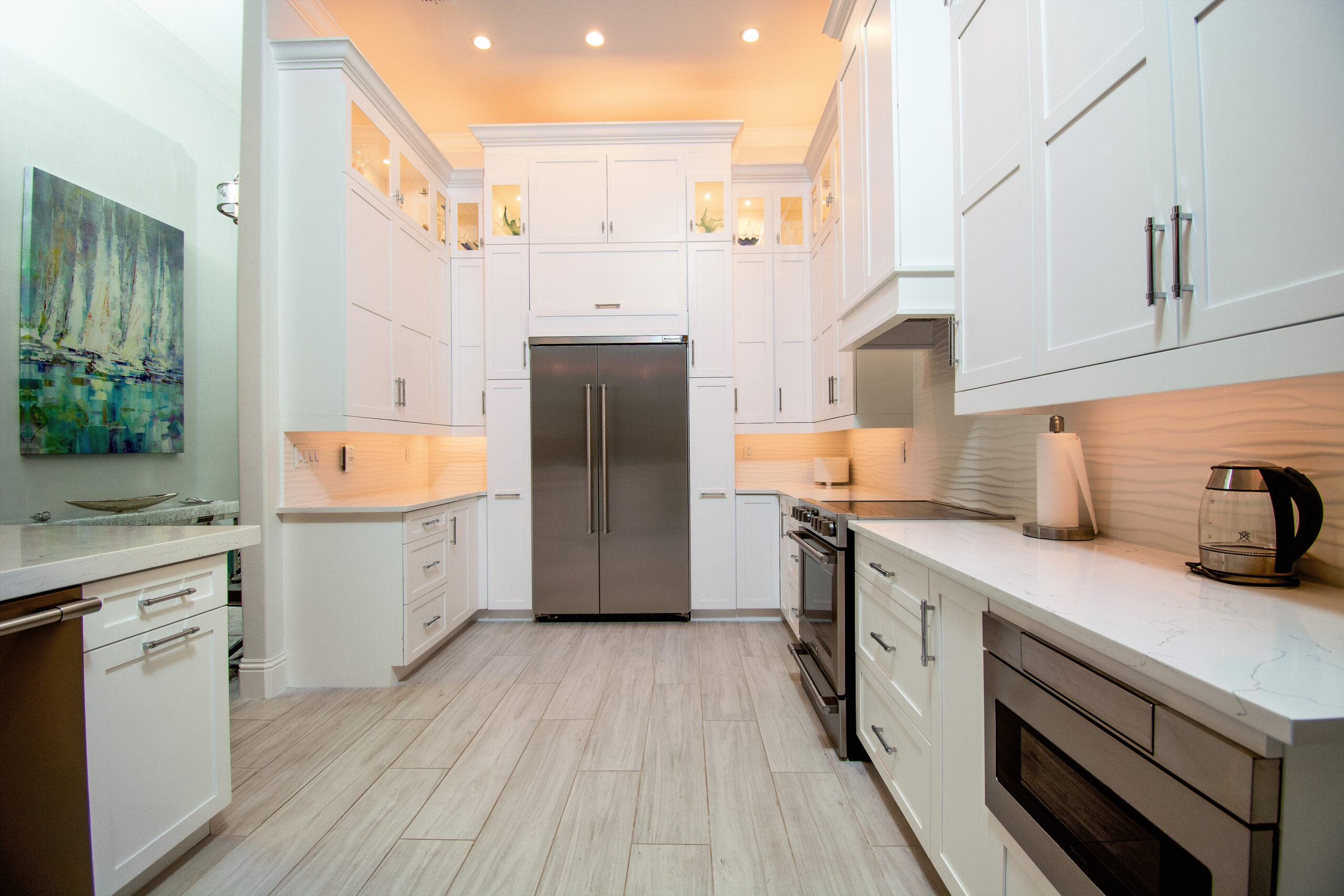 Structural kitchen renovation in Pelican Bay, Naples, with full-height white shaker cabinetry and lit glass uppers